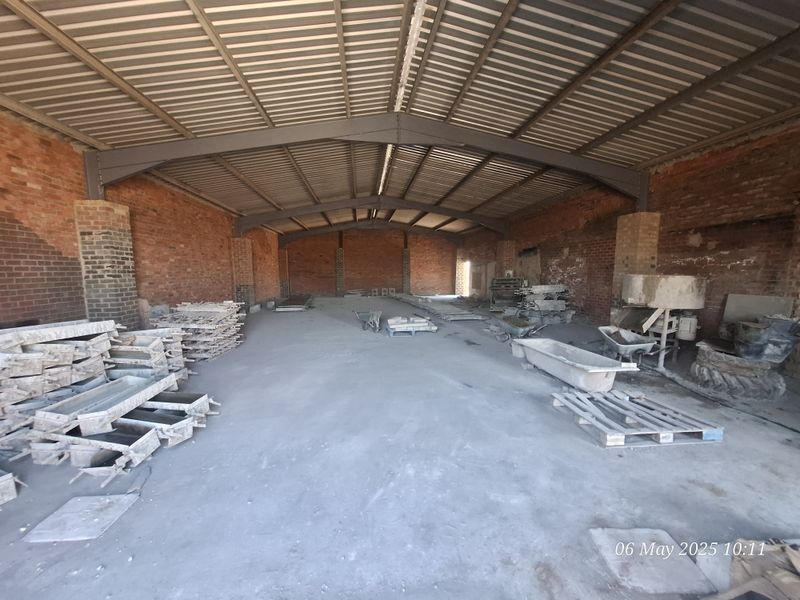 A large, open-plan industrial utility space featuring exposed brick walls, a steel portal frame, and a corrugated metal roof with a concrete floor.