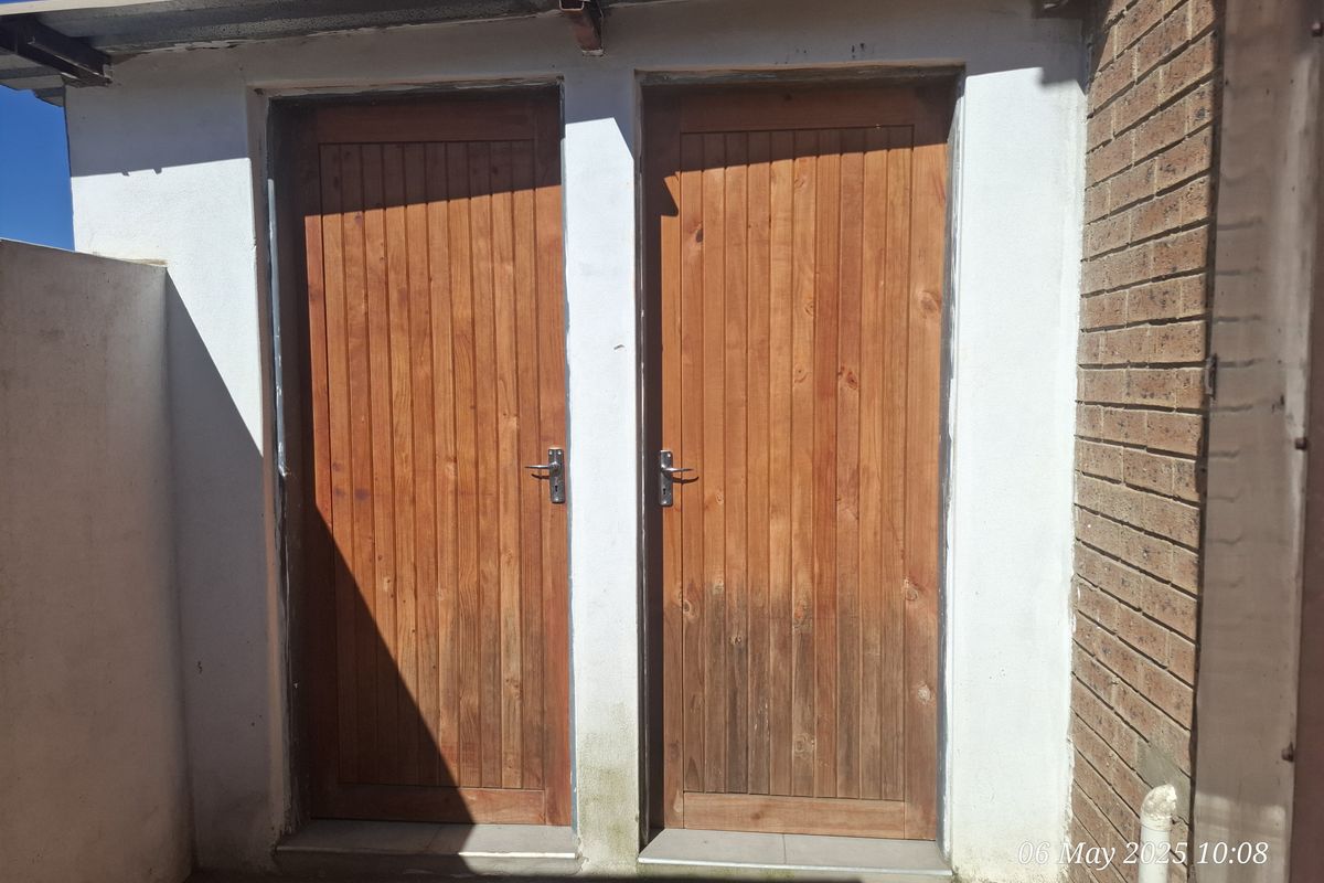 Exterior view of two timber doors set within a brick and plastered wall structure, showing signs of weathering.