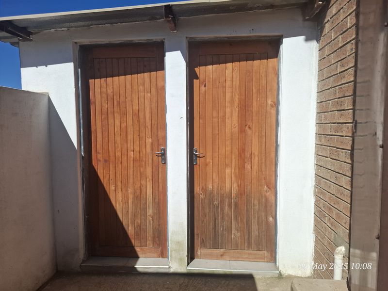 Exterior view of two timber doors set within a brick and plastered wall structure, showing signs of weathering.