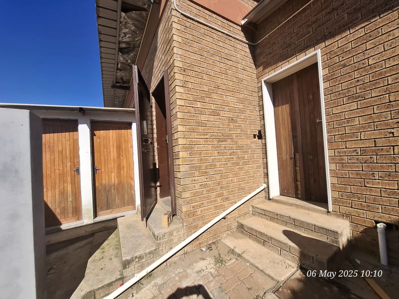 Rear exterior view of an industrial property featuring face brick walls, multiple timber access doors, and concrete steps with visible signs of weathering.