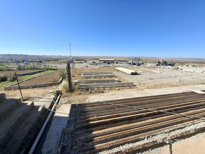 An expansive industrial outdoor area featuring concrete drainage channels, structural beams, and open land, suitable for development or storage purposes.