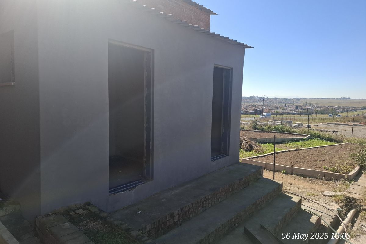 Rear exterior view of an industrial property featuring concrete steps and unfinished door frames, set against a rural landscape.