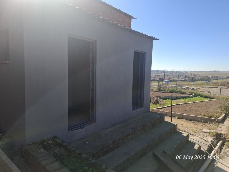 Rear exterior view of an industrial property featuring concrete steps and unfinished door frames, set against a rural landscape.