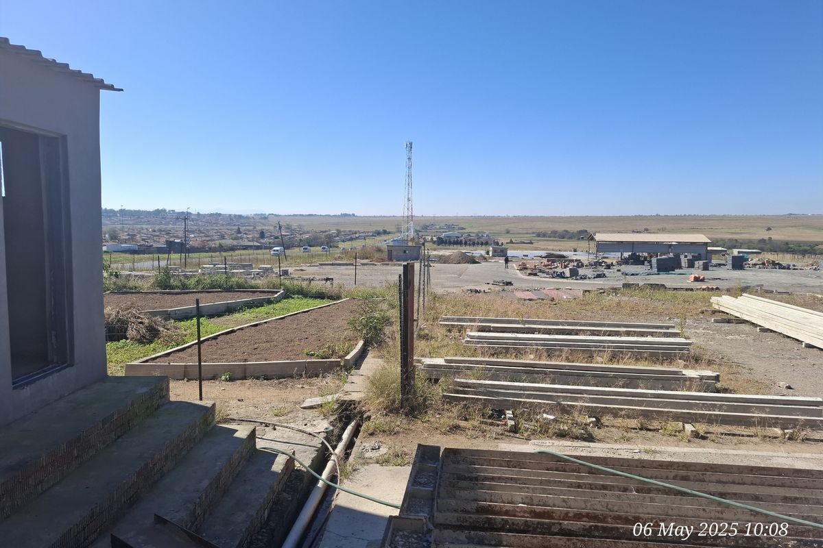 An exterior view of the industrial property grounds, featuring concrete steps, raised garden beds, and an expansive open yard area with surrounding landscape.