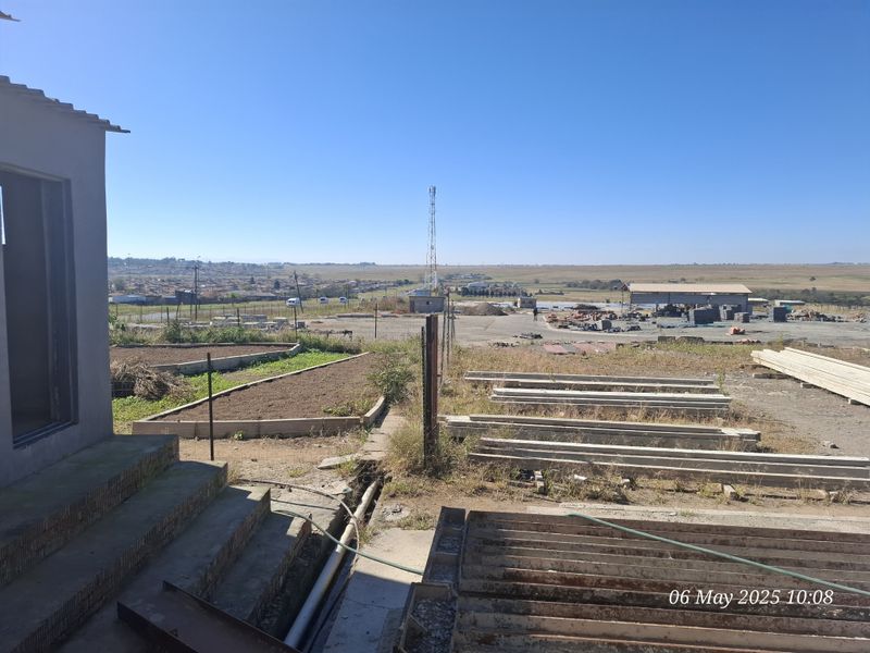 An exterior view of the industrial property grounds, featuring concrete steps, raised garden beds, and an expansive open yard area with surrounding landscape.
