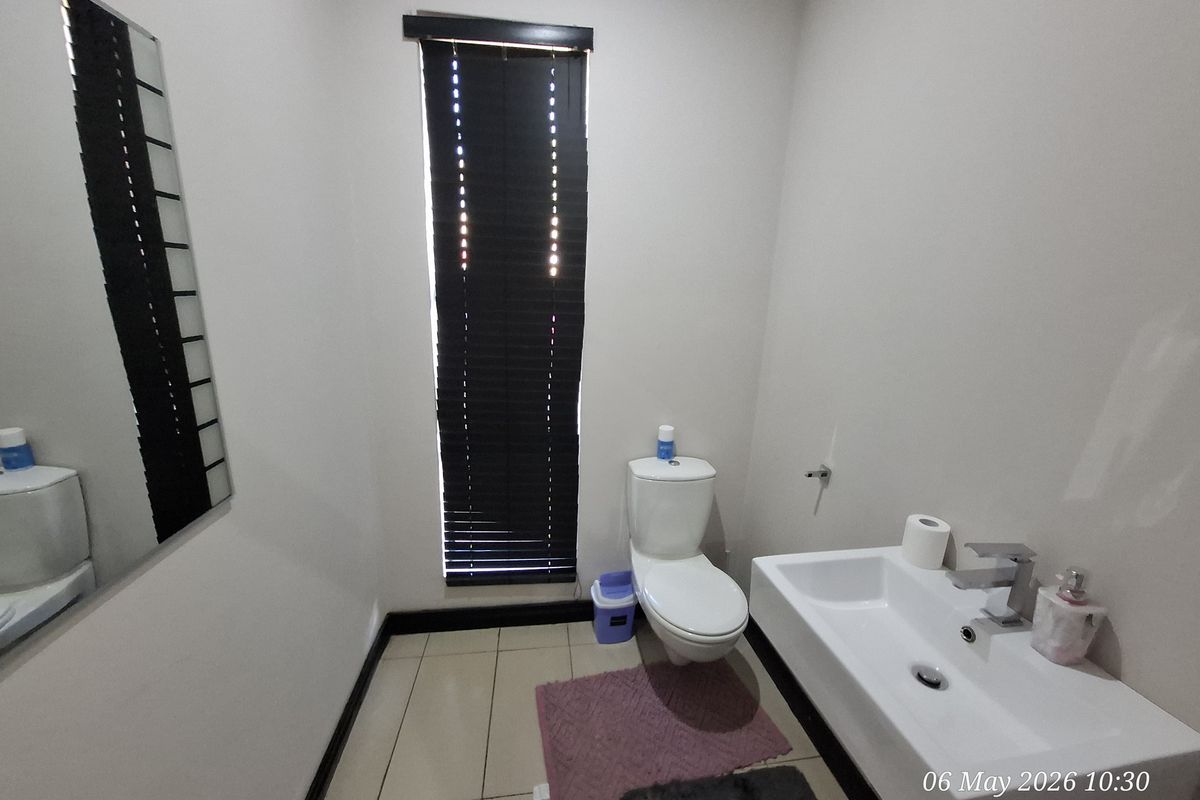 A clean and functional office restroom featuring a modern wall-mounted basin, a standard toilet, and a window with fitted blinds.