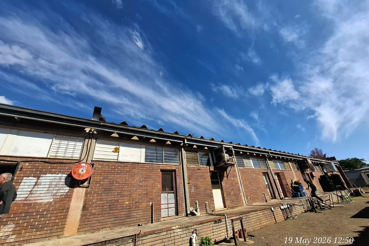 Exterior view of a commercial building featuring a brick facade, raised loading platform, and industrial window frames under a clear blue sky.