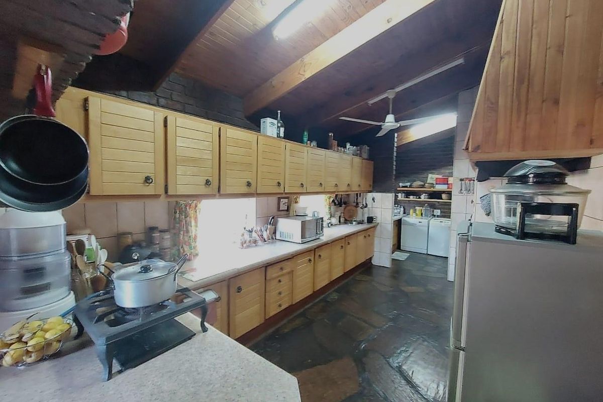 A rustic kitchen featuring timber cabinetry, stone flooring, and a vaulted timber ceiling, with an adjoining scullery area.
