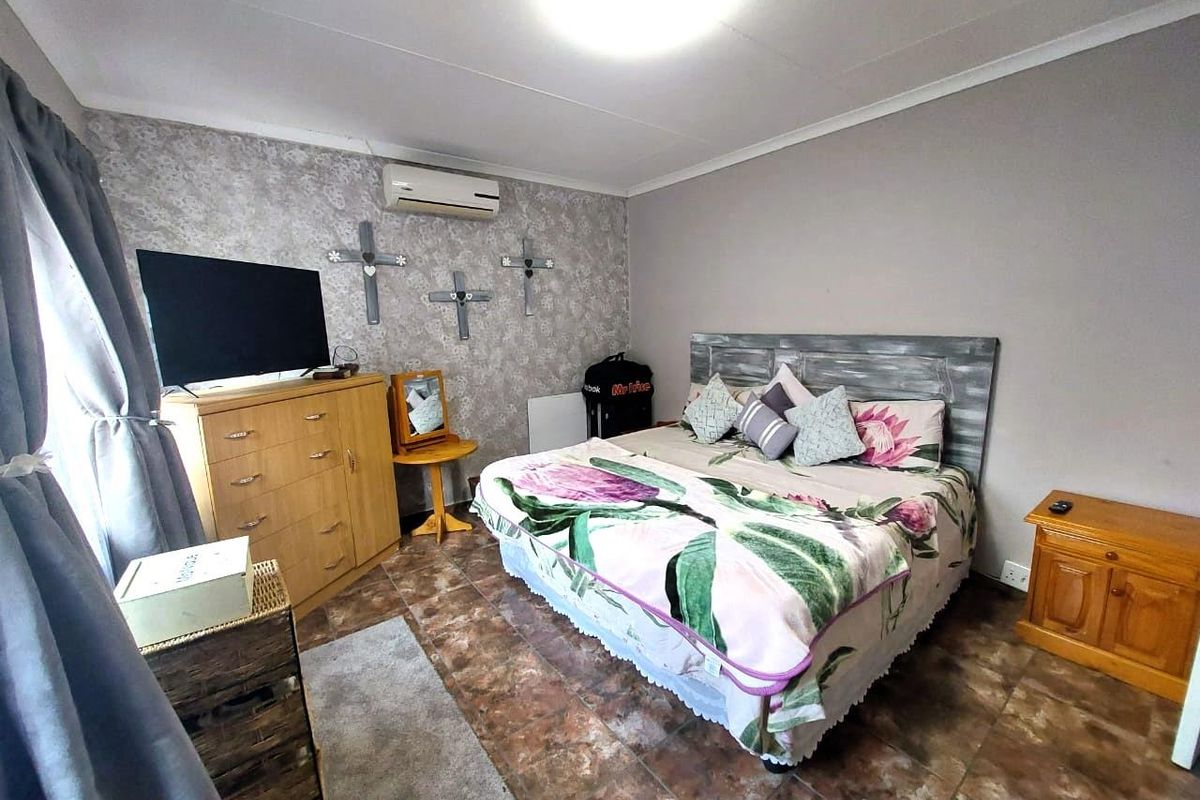 A bedroom featuring tiled flooring, a wall-mounted air conditioning unit, and a feature wall with patterned wallpaper.