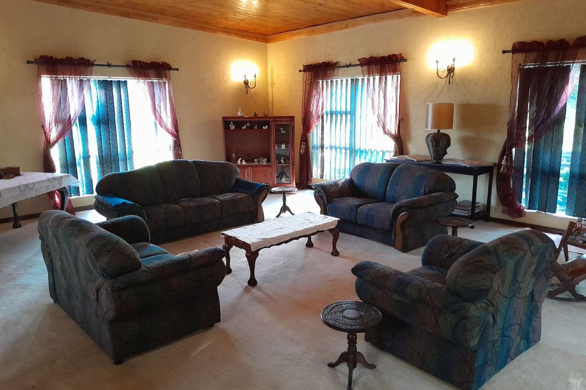 Spacious living room featuring a high timber-paneled ceiling, wall-mounted sconce lighting, and large windows with vertical blinds.
