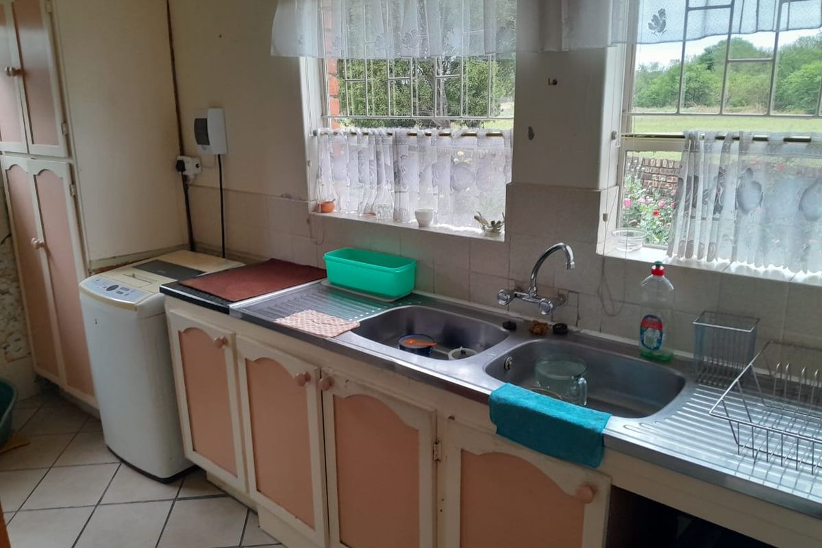 A functional kitchen area featuring a double stainless steel sink, tiled splashback, and built-in cabinetry with space for laundry appliances.