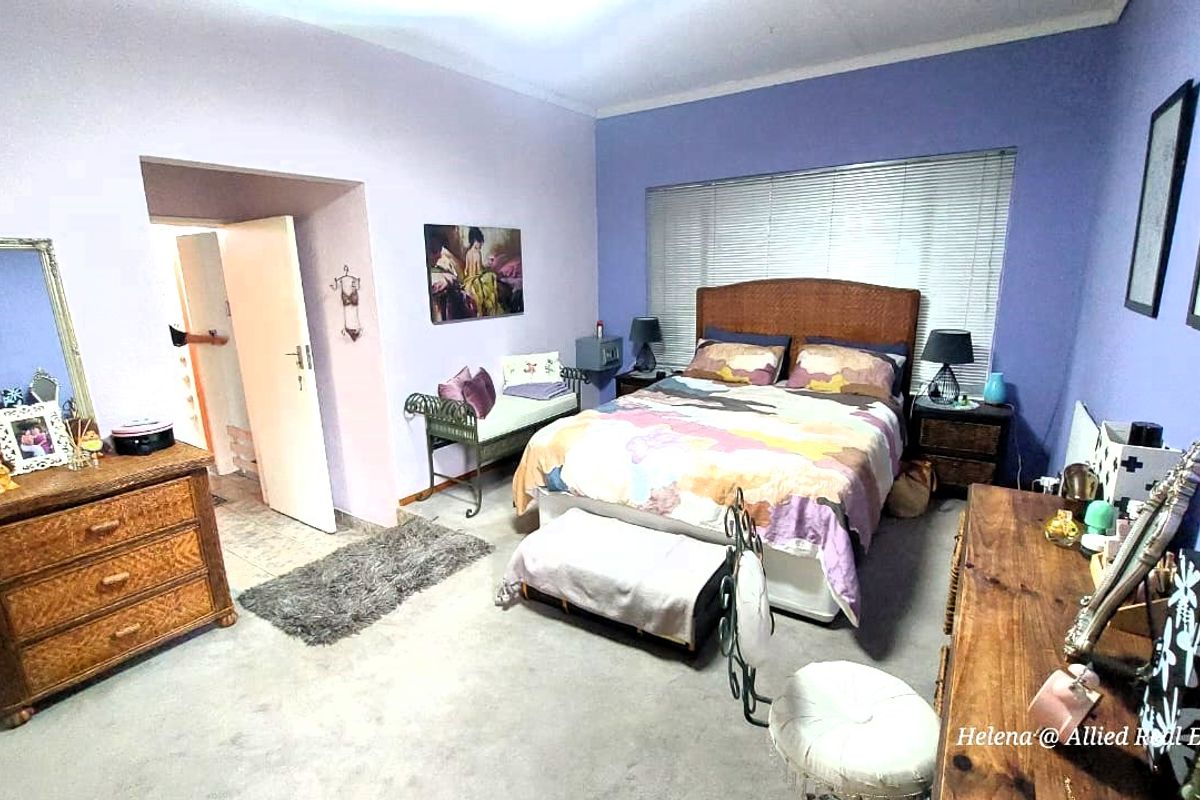 A spacious bedroom featuring neutral carpeting, dual-tone painted walls, and a large window with fitted blinds, providing a functional and comfortable sleeping area.