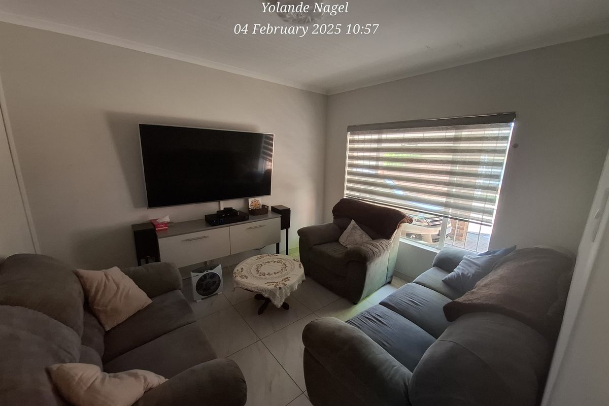 A comfortable living room featuring tiled flooring and large windows with fitted blinds, providing a bright and functional space for relaxation.