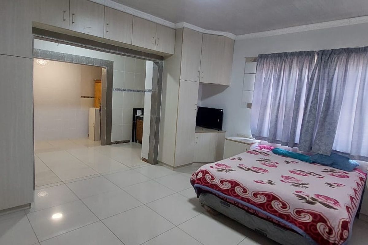Spacious bedroom featuring extensive built-in cabinetry, tiled flooring, and an open-plan layout connecting to an adjacent tiled living or utility area.