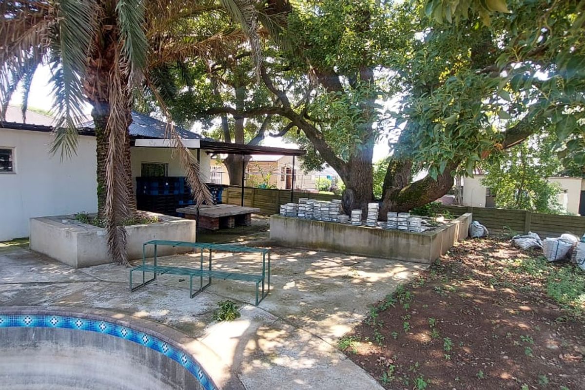 Rear garden area featuring a swimming pool, concrete patio space, mature trees, and perimeter fencing.