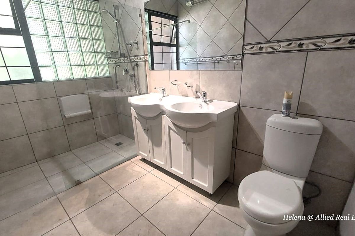 A functional bathroom featuring a double vanity with white cabinetry, a glass-enclosed shower, and a toilet, finished with neutral wall and floor tiles.