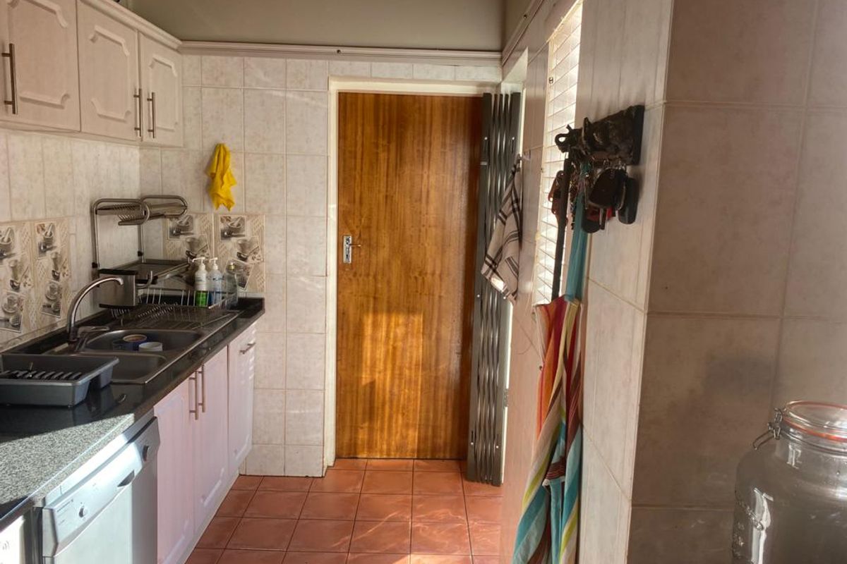 A functional kitchen featuring tiled walls, built-in cabinetry, a stainless steel sink, and tiled flooring with direct access to an adjacent area.
