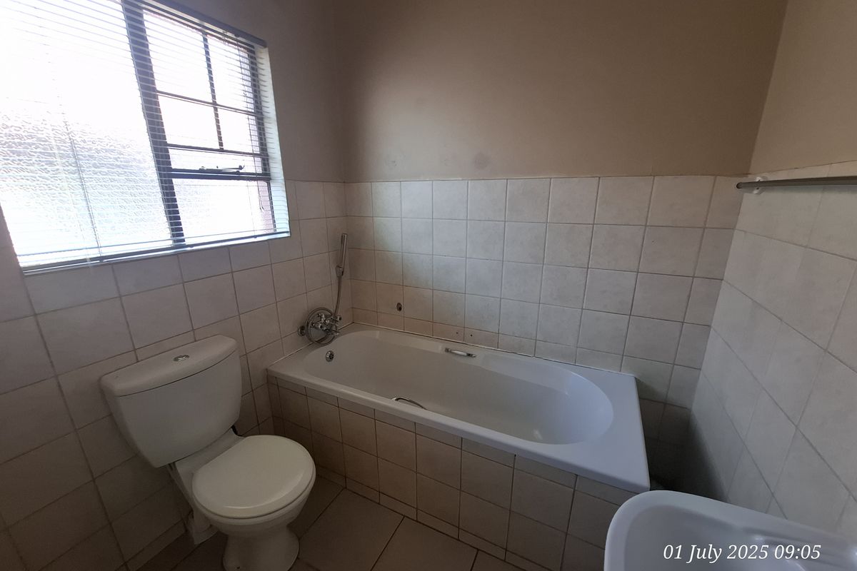 A functional bathroom featuring a built-in bathtub with shower mixer, a standard toilet, and tiled walls and flooring.