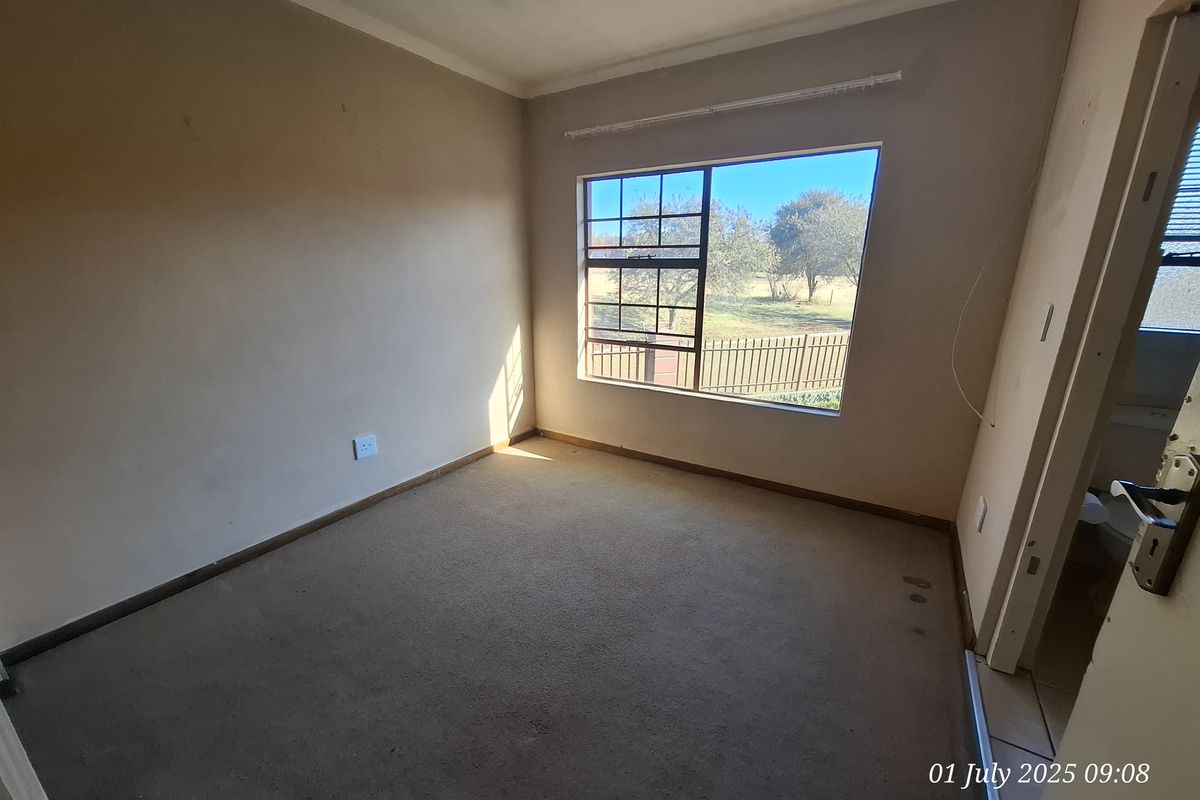 An empty bedroom featuring carpeted flooring, a large window with exterior views, and neutral wall finishes, ready for renovation or personalization.