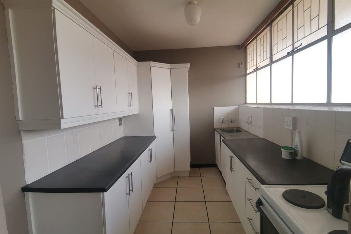 A functional kitchen featuring white built-in cabinetry, dark laminate countertops, tiled splashbacks, and large windows providing ample natural light.