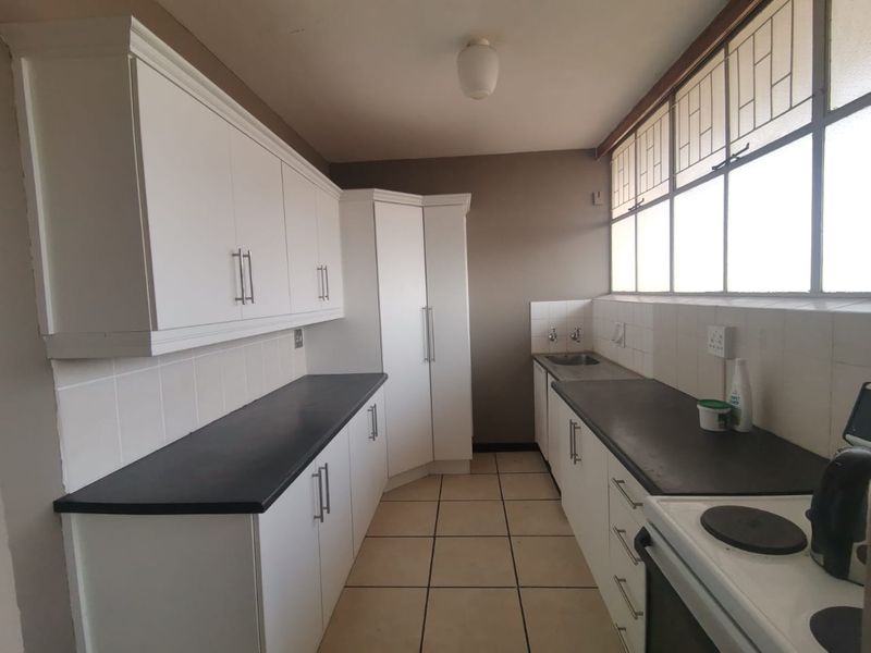 A functional kitchen featuring white built-in cabinetry, dark laminate countertops, tiled splashbacks, and large windows providing ample natural light.