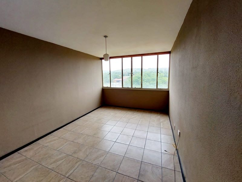 An empty bedroom featuring tiled flooring, neutral walls, and a large window providing natural light and exterior views.