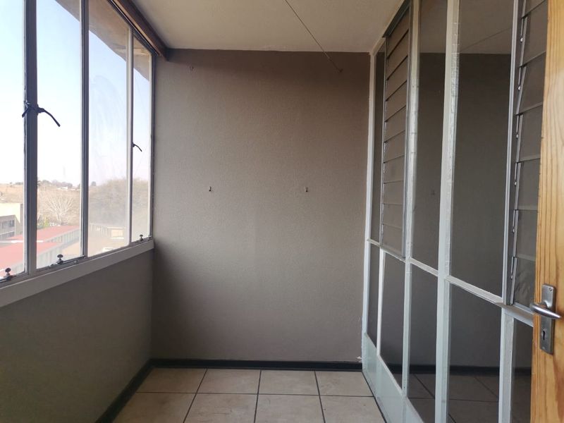 An enclosed balcony featuring tiled flooring and large aluminium-framed windows, offering a versatile space that can be used as a sunroom or study area.