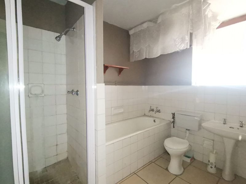 A functional bathroom featuring a separate shower enclosure, built-in bathtub, pedestal basin, and toilet, with neutral wall and floor tiling throughout.