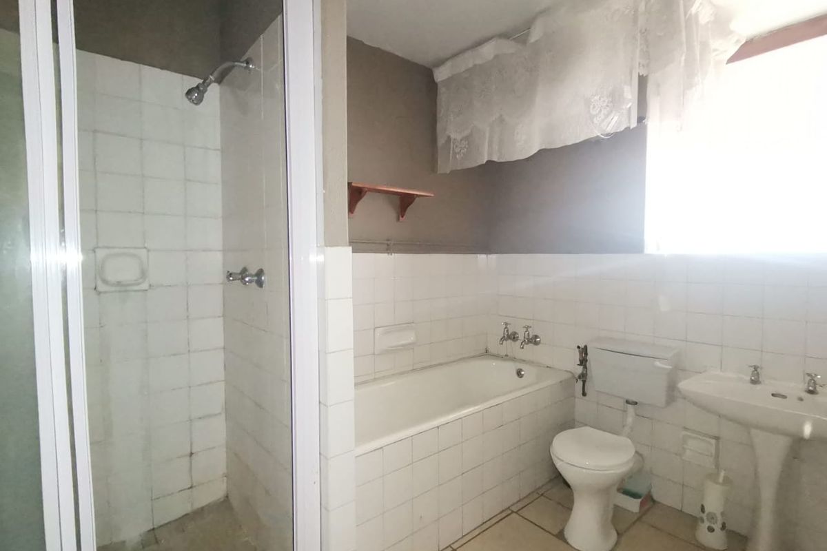 A functional bathroom featuring a separate shower enclosure, built-in bathtub, pedestal basin, and toilet, with neutral wall and floor tiling throughout.