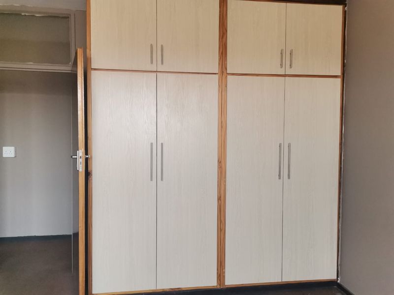 A bedroom featuring floor-to-ceiling built-in cupboards with light wood-grain finish doors and modern metal handles.