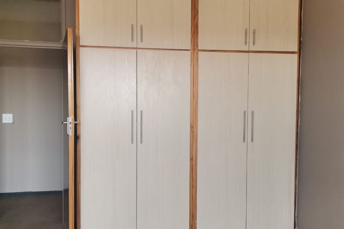 A bedroom featuring floor-to-ceiling built-in cupboards with light wood-grain finish doors and modern metal handles.