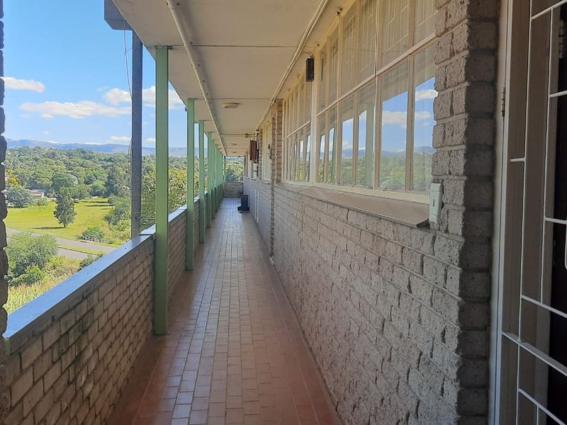 An open-air balcony walkway featuring brick walls, tiled flooring, and metal support columns, offering an elevated view of the surrounding landscape.