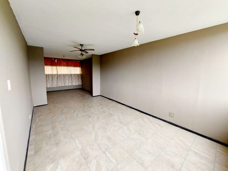 A spacious, empty living area featuring neutral tiled flooring, a ceiling fan, and pendant lighting, offering a blank canvas for personalization.
