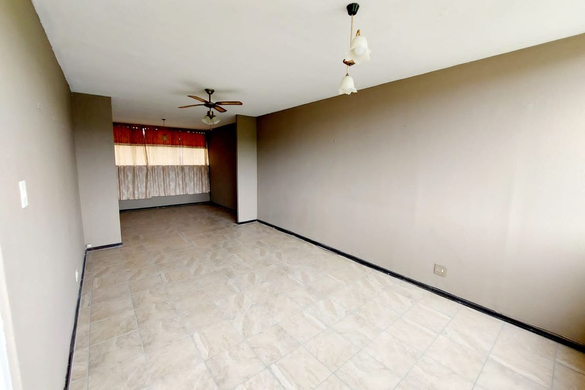 A spacious, empty living area featuring neutral tiled flooring, a ceiling fan, and pendant lighting, offering a blank canvas for personalization.