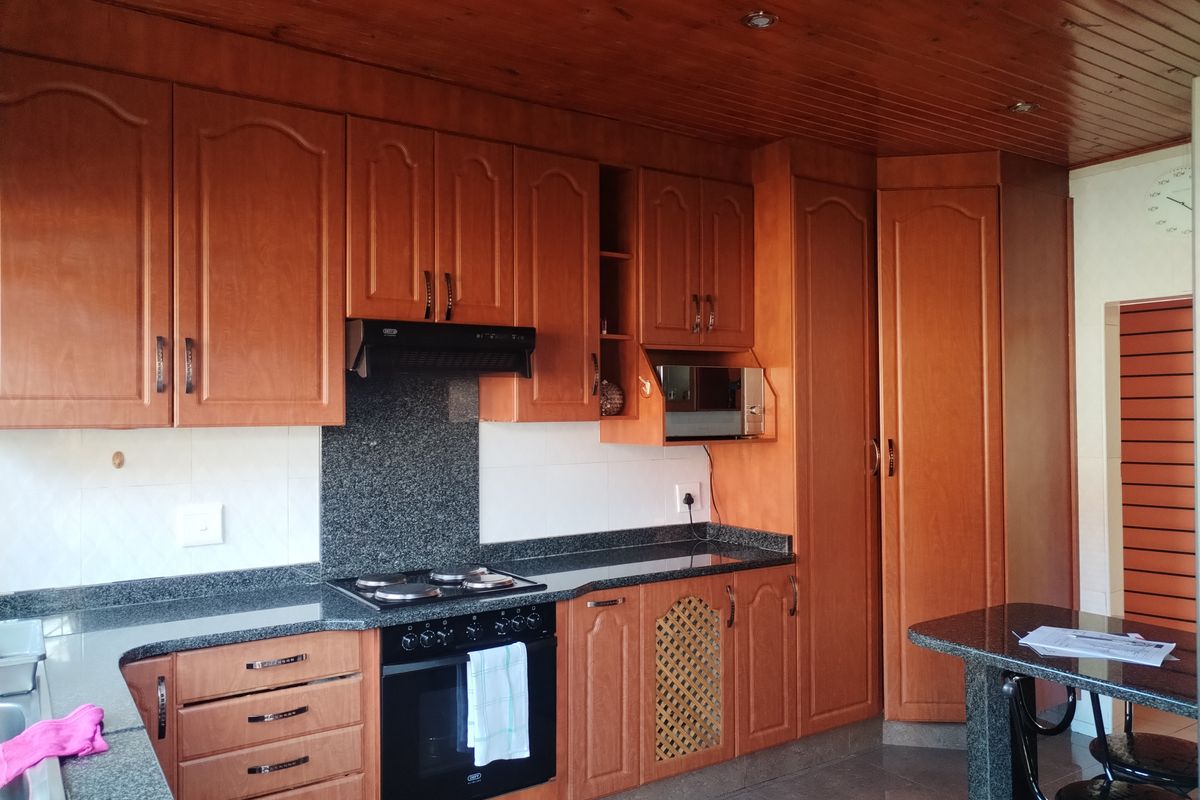 A functional kitchen featuring wood-finish cabinetry, granite countertops, a built-in oven with hob, and a wood-paneled ceiling.