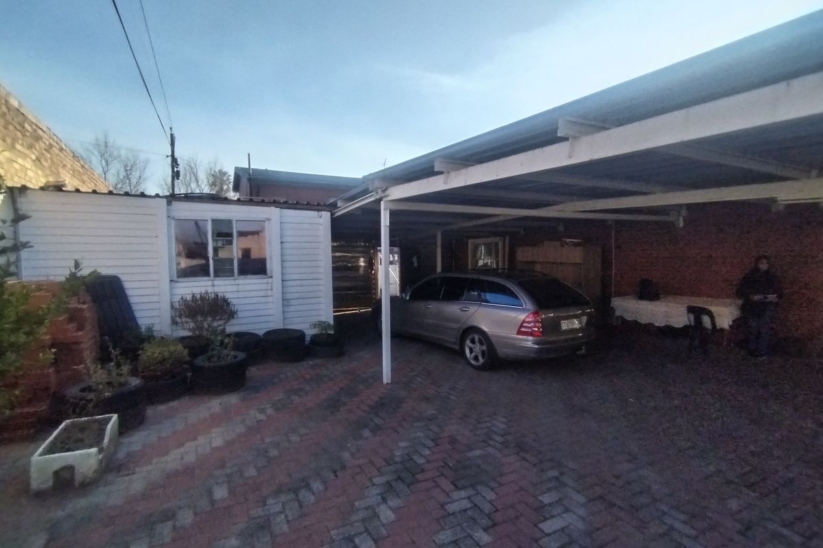 An exterior view of a property featuring a paved driveway area with a covered carport structure and adjacent exterior wall finishes.