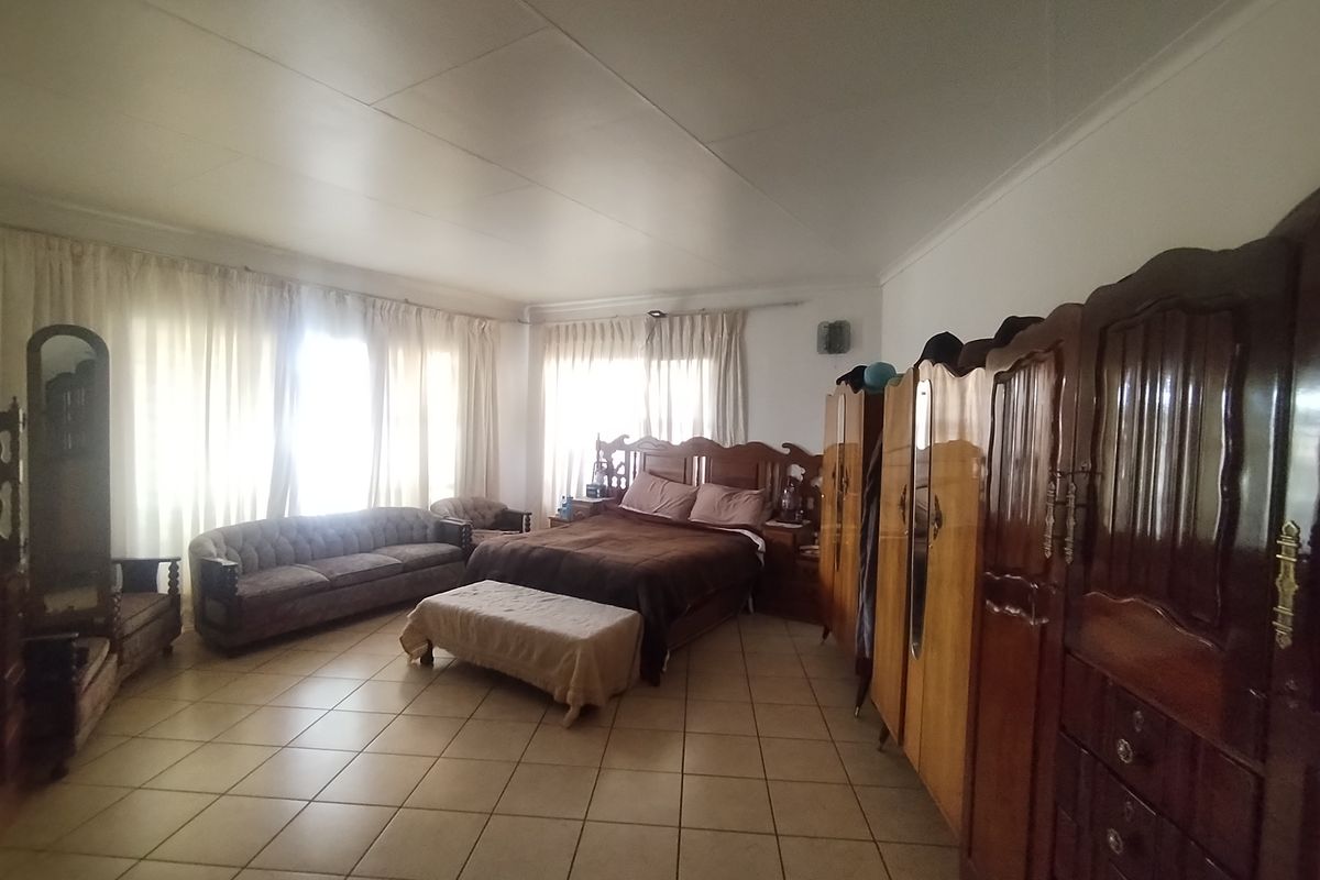Spacious bedroom featuring tiled flooring and large windows with curtain treatments, offering a functional layout with ample room for furniture.