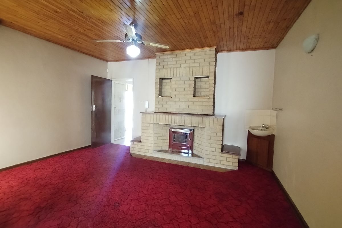 A living room featuring a prominent brick fireplace with an integrated stove, wood-paneled ceiling, and a small corner vanity basin.