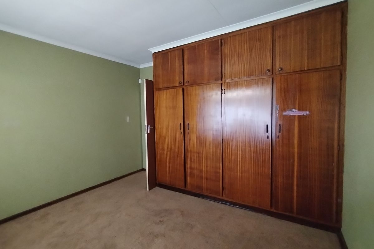 A bedroom featuring built-in wooden cupboards, green painted walls, and carpeted flooring.