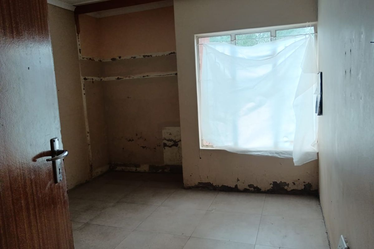 An empty bedroom featuring tiled flooring and a window, currently requiring significant cosmetic repairs and wall restoration.