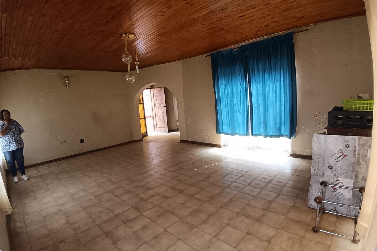 Spacious living room featuring a timber-clad ceiling, tiled flooring, and an arched doorway leading to an adjacent area.