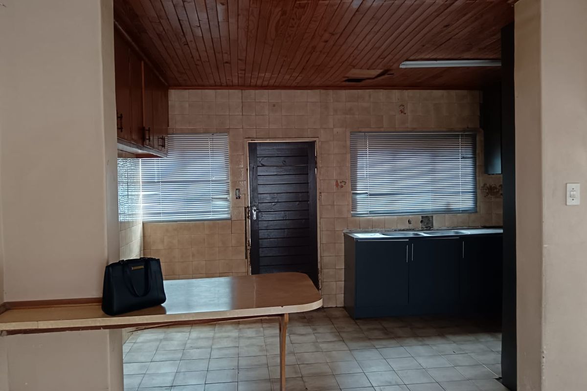 A dated kitchen featuring wood-paneled ceilings, tiled walls, built-in cabinetry, and a breakfast counter, requiring modernization to reach its full potential.