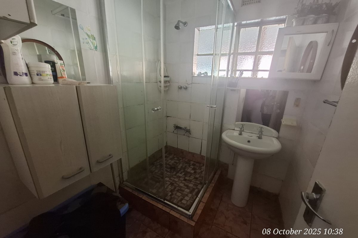 A compact bathroom featuring a glass-enclosed shower, pedestal basin, and tiled finishes throughout.