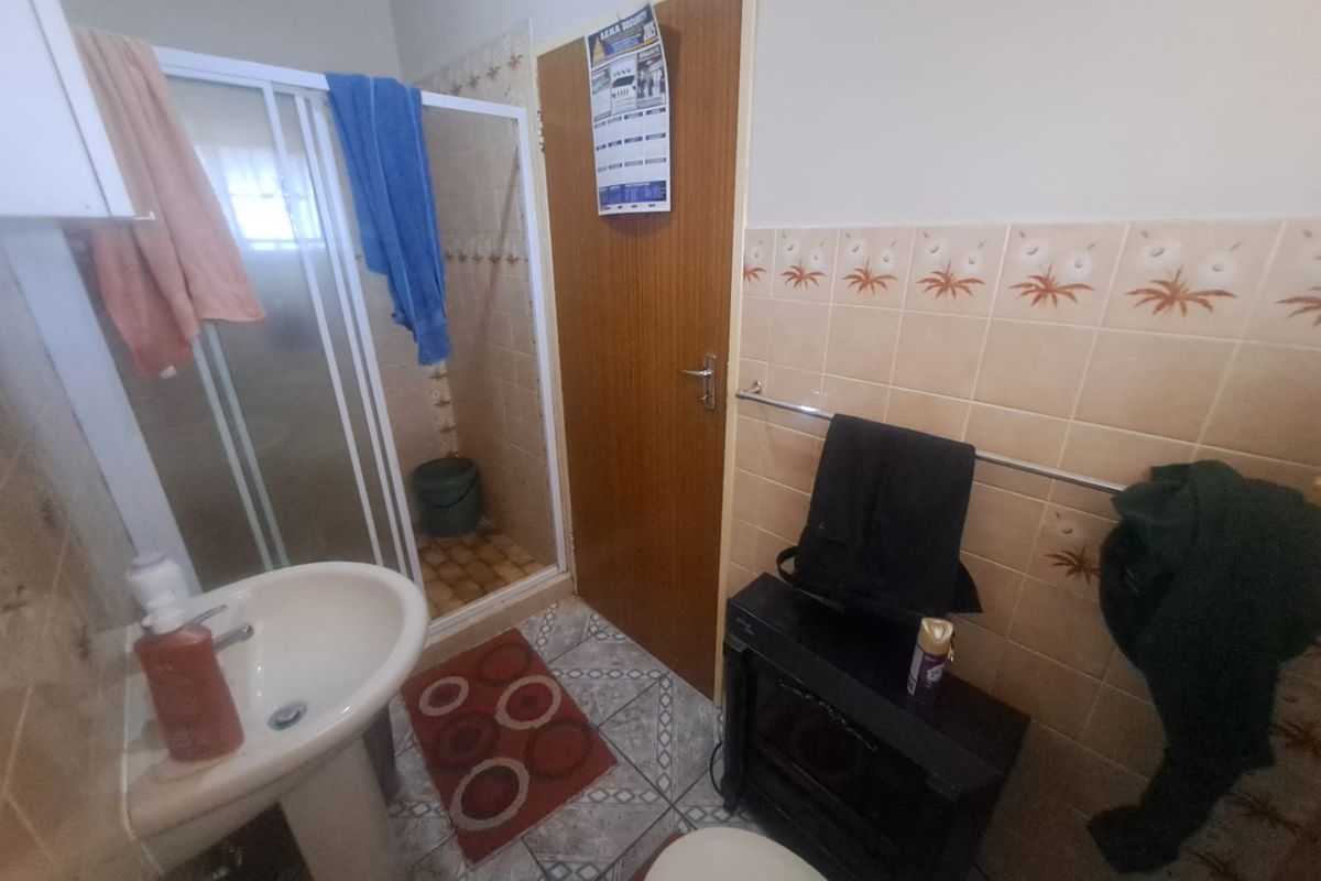 A functional bathroom featuring a shower enclosure, pedestal basin, and tiled walls, presenting an opportunity for modernization and cosmetic updates.