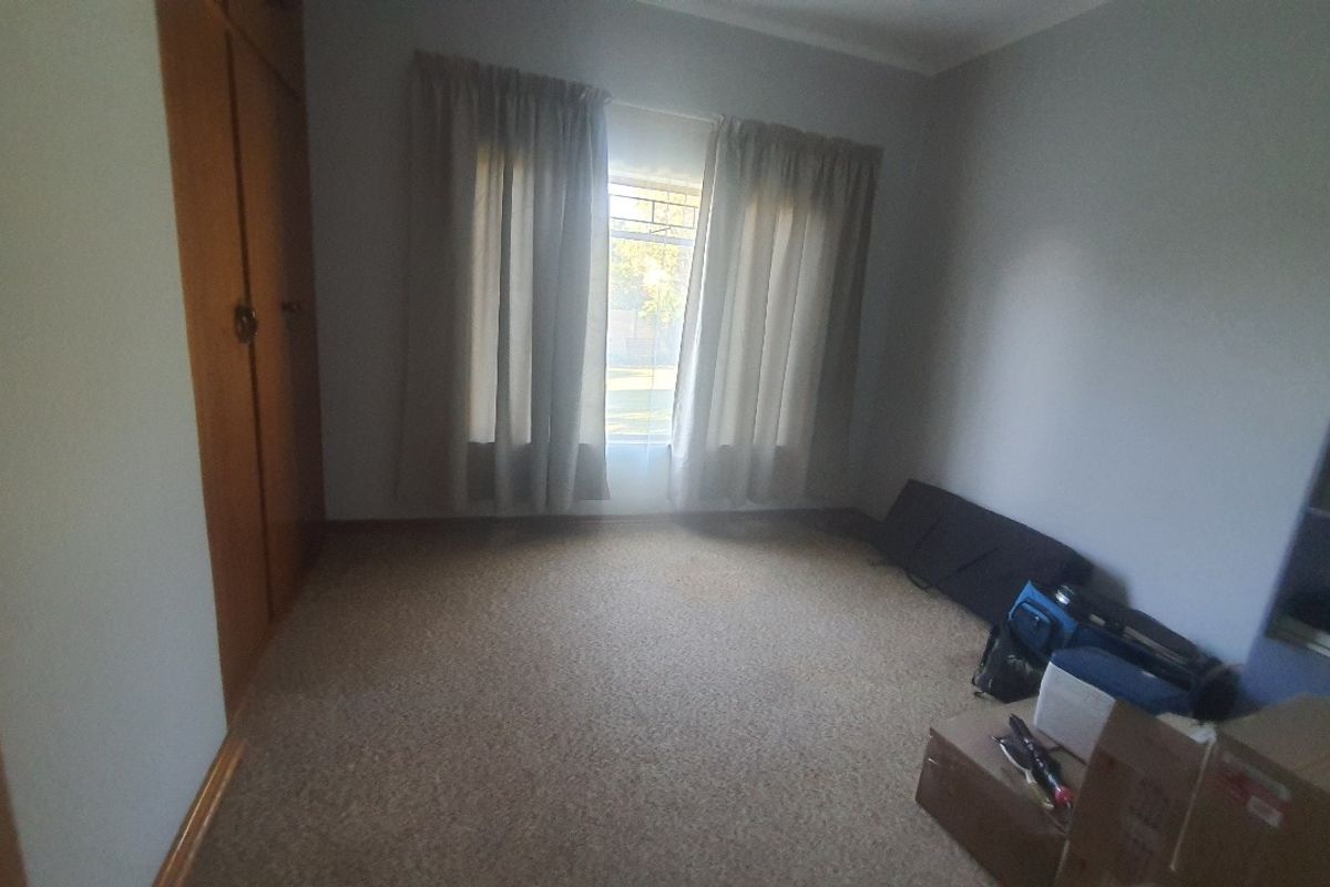 A bedroom featuring built-in wooden cupboards and carpeted flooring, offering a functional space with natural light from the window.