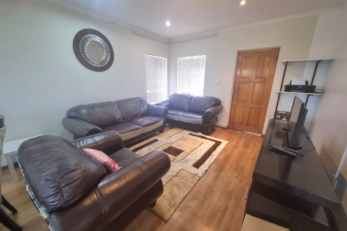 A living room featuring laminate flooring, recessed downlighting, and venetian blinds, providing a functional and neutral space.