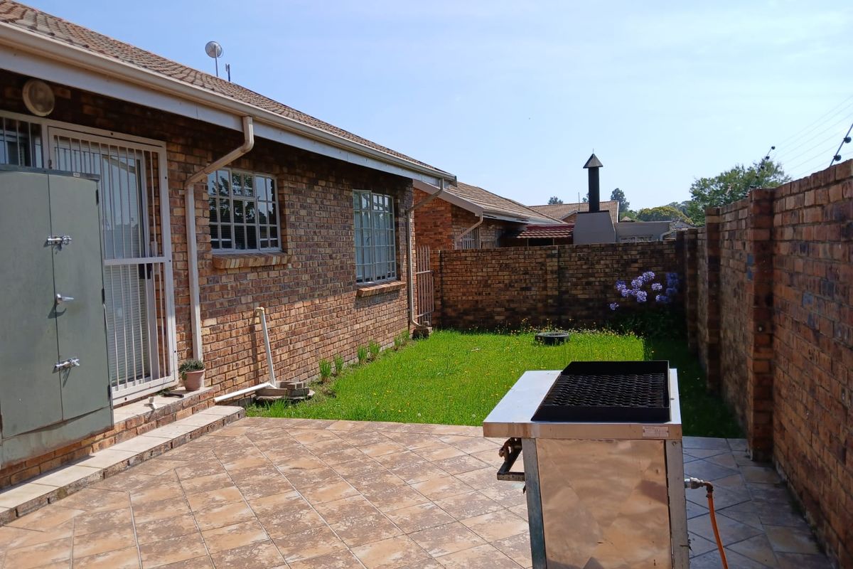 Rear exterior view of the townhouse featuring a paved patio area, private lawn, and brick boundary walls.