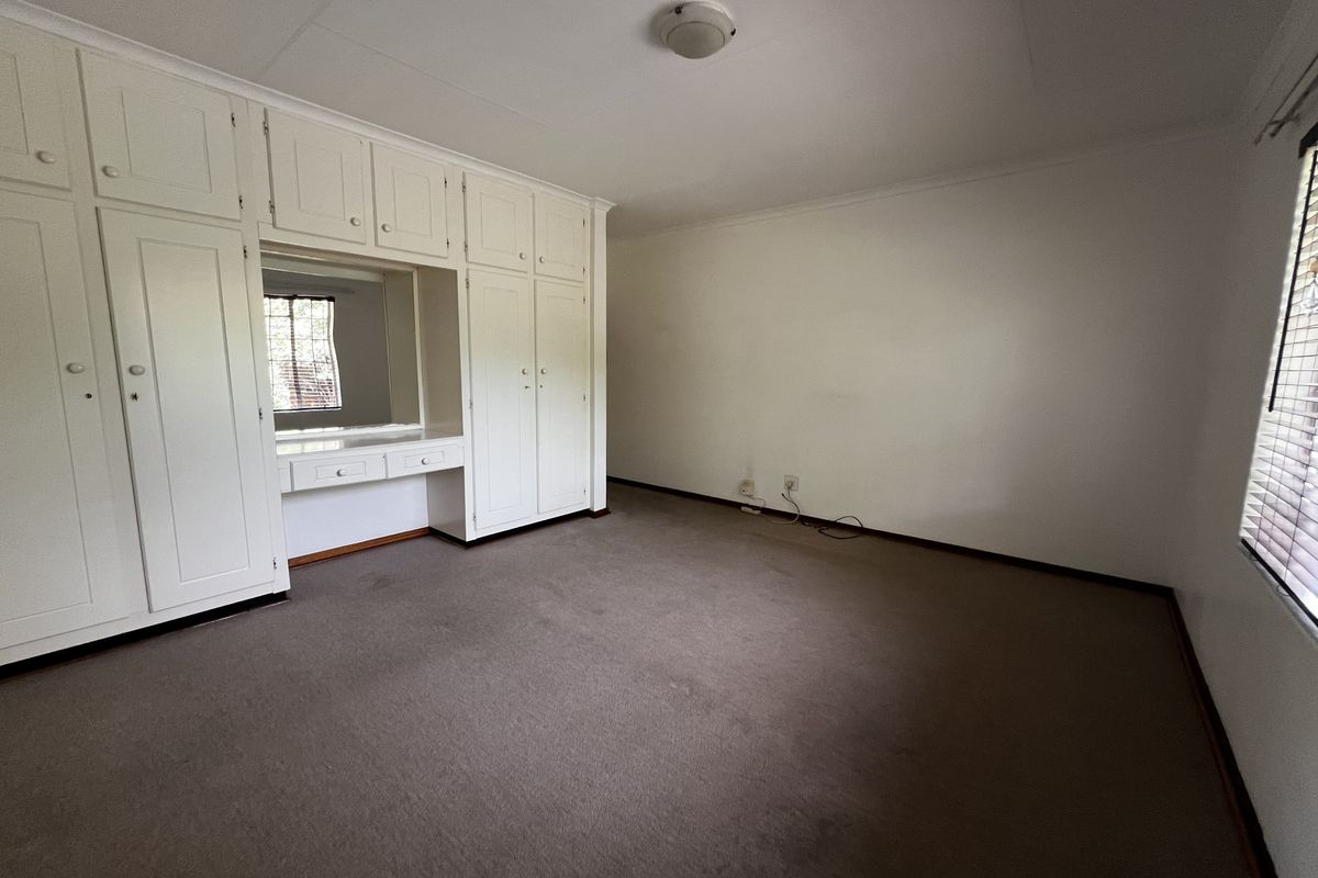 A spacious bedroom featuring extensive built-in white cabinetry with an integrated vanity area, neutral carpeting, and large windows allowing natural light.