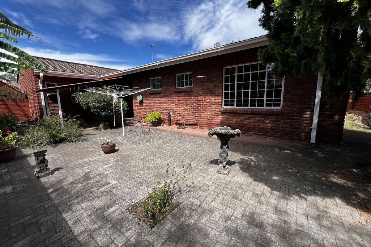 A rear exterior view of the townhouse featuring a paved courtyard area, brick facade, and established garden surroundings.