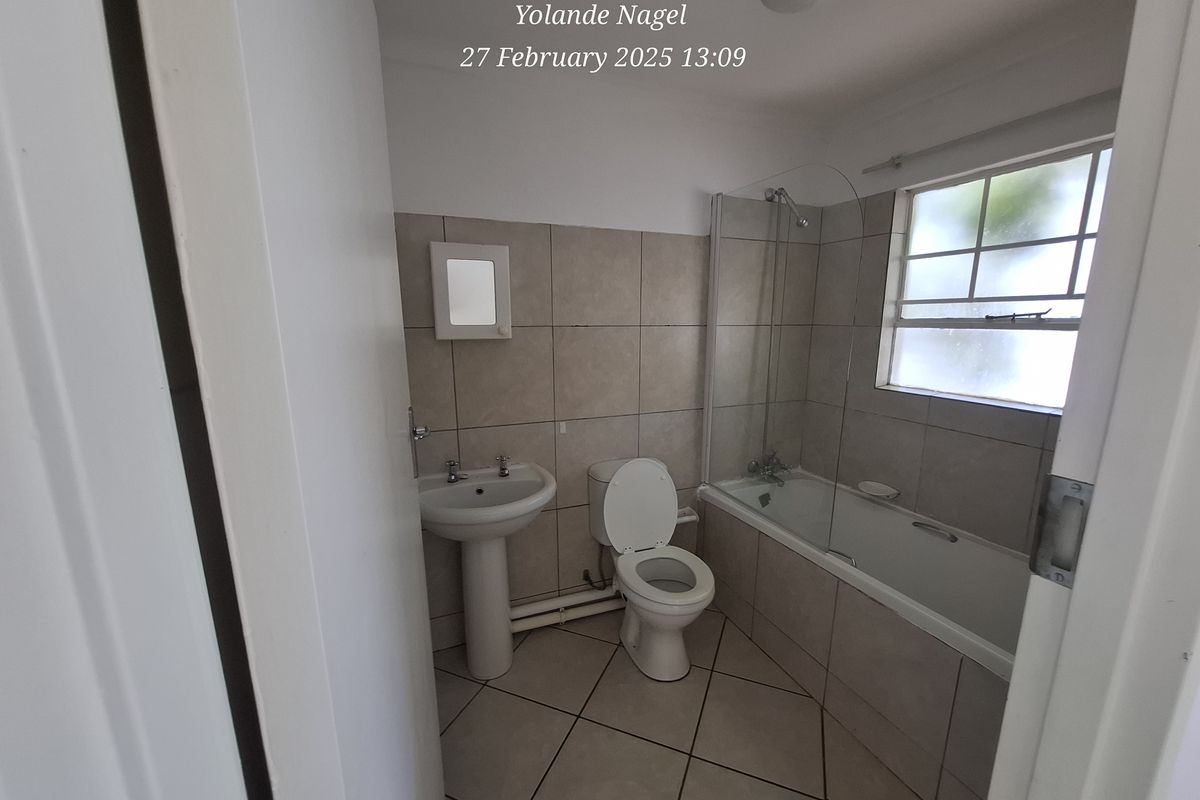 A functional bathroom featuring a pedestal basin, toilet, and a bathtub with an integrated shower screen and tiled surround.